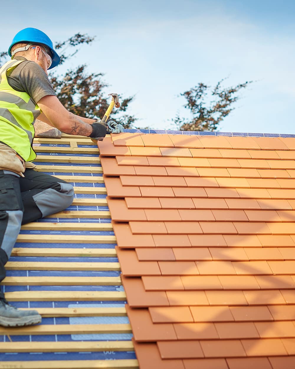 A roofer laying a new course of clay tiles on treated battens